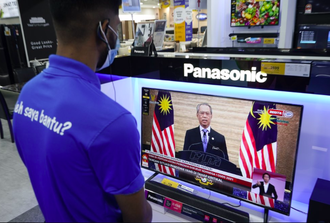 Malaysia ban bố tình trạng khẩn cấp, thủ tướng tạm thoát nguy cơ mất chức Nhân viên một cửa hàng điện tử ở Kuala Lumpur xem Thủ tướng Muhyiddin phát biểu trên truyền hình ngày 12/1. (Ảnh: AP)