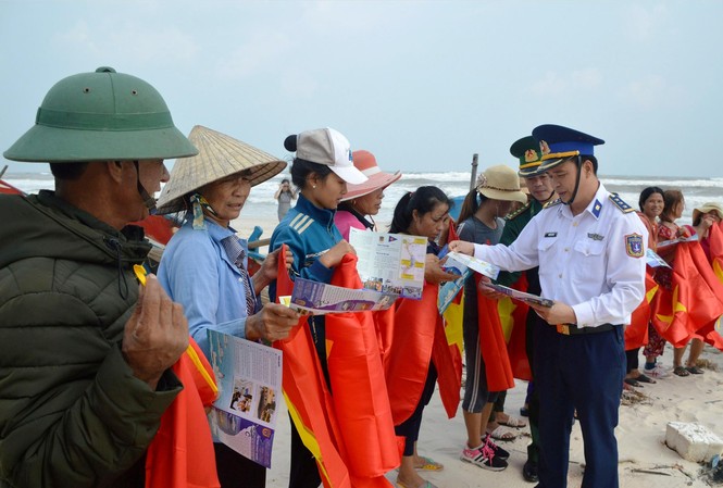 Cảnh sát biển chung tay tháo gỡ 'thẻ vàng' EC Vùng CSB 1 tặng cờ Tổ quốc và cấp phát tờ rơi tuyên truyền cho bà con ngư dân ở huyện Lệ Thủy (Quảng Bình). Ảnh: M.T