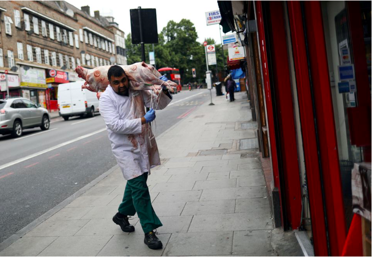 Một người đàn ông vác con lợn vào cửa hàng bán thịt ở London. (Ảnh: Reuters)