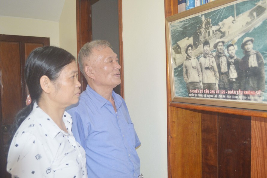 Bên bức ảnh tàu C235 treo tại nhà, CCB Lê Duy Mai kể cho chị Doãn Thị Thu về trận chiến đấu dũng cảm năm xưa của các đồng đội. Ảnh: Kiến Nghĩa