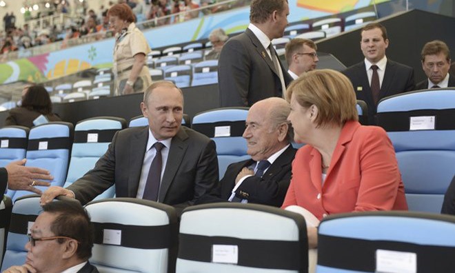Bà Merkel trò chuyện với Tổng thống Nga Vladimir Putin (trái) và Chủ tịch FIFA (giữa) trên hàng ghế khán đài sân vận động.