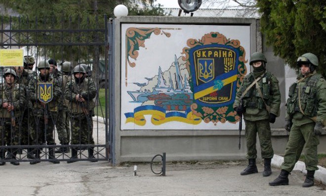 Binh lính Ukraine (trái) và các tay súng không rõ danh tính (phải) đứng ở cổng một doanh trại quân đội Ukraine ở Perevalnoye.